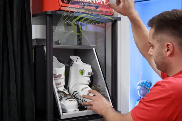 Mężczyzna w czerwonej koszulce ogląda białe buty narciarskie Fischer w sklepie.