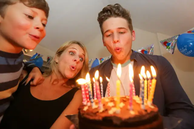 Rodzina zdmuchuje świeczki z tortu urodzinowego.
