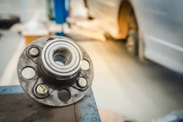 Nowe łożysko koła czeka na montaż. W tle widać podniesiony samochód, gotowy do naprawy.