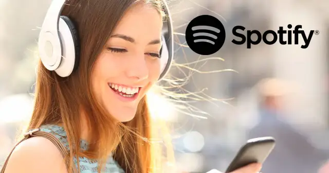 Uśmiechnięta kobieta w słuchawkach słucha czegoś na telefonie, obok logo Spotify.