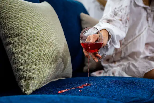 Wino rozlane na granatową kanapę. Jasna poduszka obok, a na niej plamy. Idealne tkaniny obiciowe łatwe do czyszczenia.