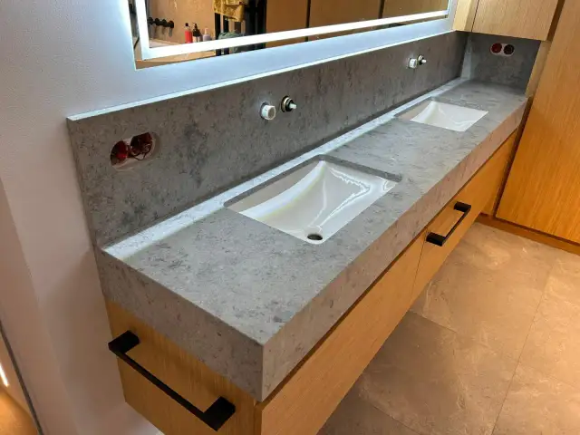 Łazienka z dwoma umywalkami nablatowymi, blatem z konglomeratu kwarcowego i drewnianymi szafkami.