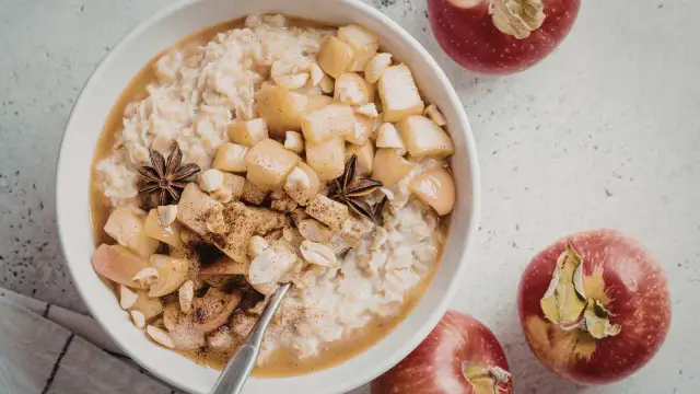 Miseczka owsianki z jabłkami, orzechami i anyżem, obok czerwone jabłka.