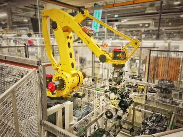 Żółty robot przemysłowy FANUC M-410iC pracuje nad montażem silnika, uosabiając filozofię kaizen toyota w nowoczesnej fabryce.