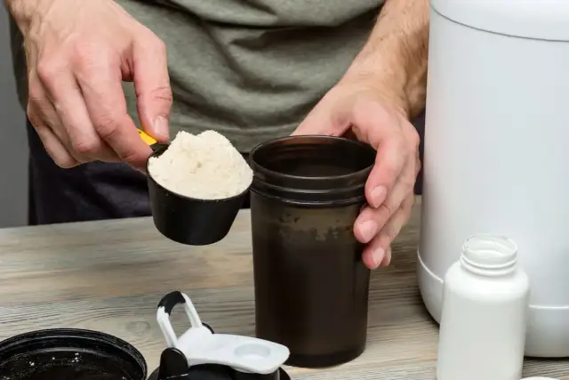Mężczyzna wsypuje proszek z miarki do shakera.