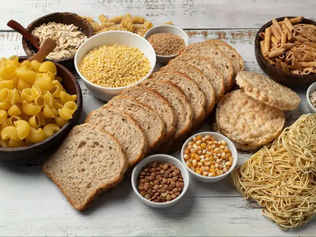 W czym są węglowodany? Na stole leżą płatki owsiane, makarony, pieczywo, ryż, soczewica i kukurydza.