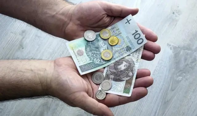 Dłonie trzymające polskie banknoty 100 zł i 10 zł oraz monety.