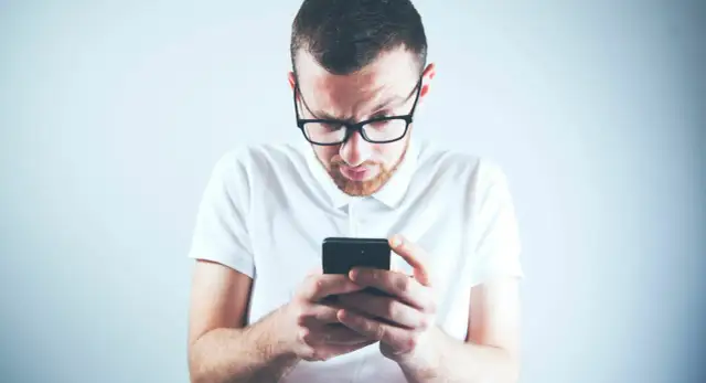 Zastanawiasz się, skąd firma windykacyjna ma Twój numer telefonu? Mężczyzna w okularach patrzy zdezorientowany na ekran smartfona.