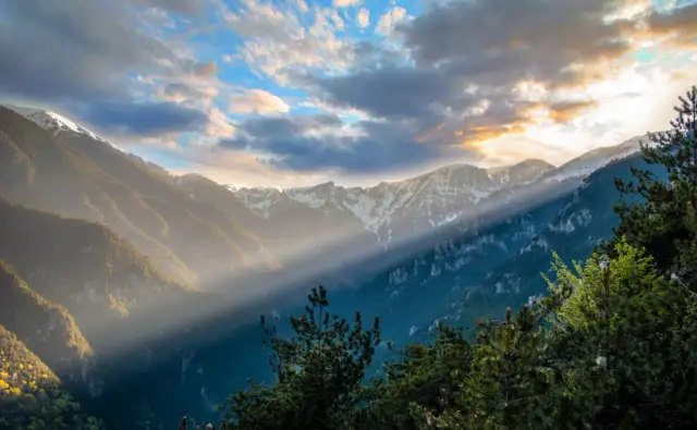 Promienie słońca przebijają się przez chmury, oświetlając zbocza masywu Olimpu.