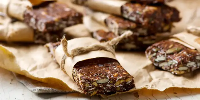 Domowe batony proteinowe z nasionami i bakaliami, zawinięte w papier i przewiązane sznurkiem. Idealne, gdy zastanawiasz się, jakie batony proteinowe wybrać.