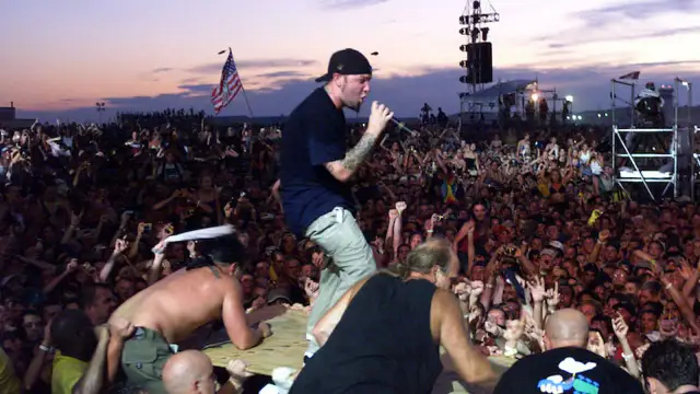 Tłum na Woodstock 99, z wokalistą na scenie i amerykańską flagą. Atmosfera była napięta, co doprowadziło do późniejszych zamieszek i ofiar.