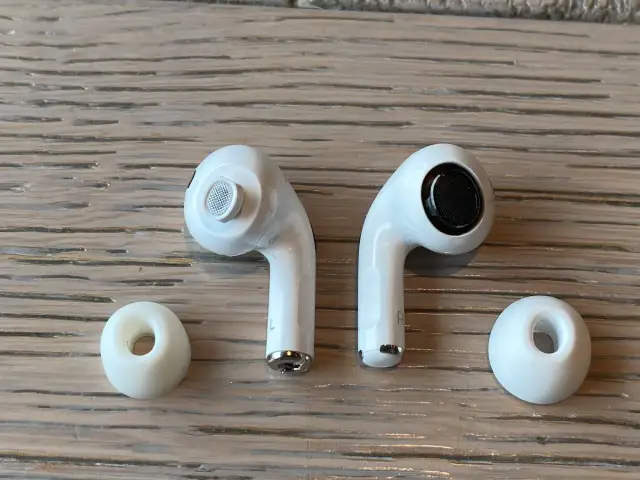 Dwa białe słuchawki AirPods i dwie gumowe nakładki na drewnianym tle.
