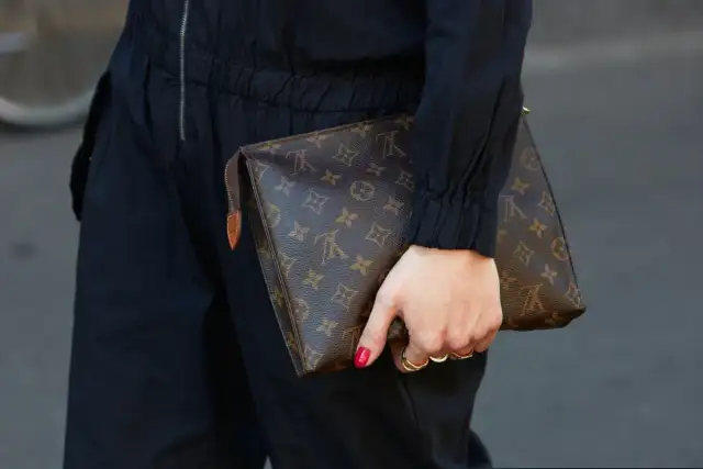 Dłoń trzyma brązową kopertówkę Louis Vuitton z monogramem.