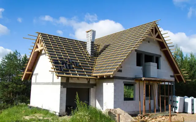 Budowa domu z białej cegły, z widoczną konstrukcją dachu i kominem.