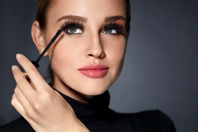 Kobieta aplikuje tusz do rzęs, tworząc efekt sztucznych rzęs dla początkujących. Długie, gęste rzęsy podkreślają jej spojrzenie.