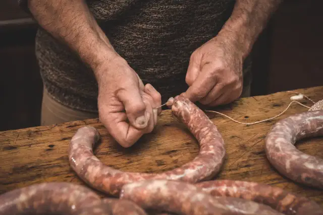 Ręce wiążą kiełbasę sznurkiem. Zastanawiasz się, jak długo wędzić kiełbasę bez parzenia?
