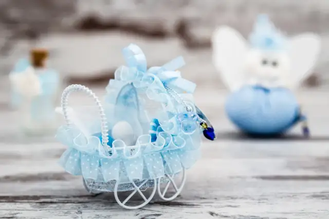 Niebieski wózek dla lalek z ozdobami, w tle aniołek i buteleczka.