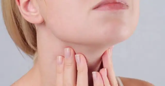 Kobieta dotyka szyi, gdzie znajduje się tarczyca. Wyniki badań wskazują na ft3 podwyższone tsh w normie, co może wymagać dalszej diagnostyki.