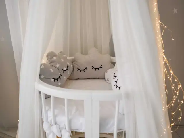 Urocze poduszki w kształcie chmurek i serca z gwiazdkami, idealne co do łóżeczka dla noworodka. Delikatny baldachim i lampki tworzą magiczną atmosferę.