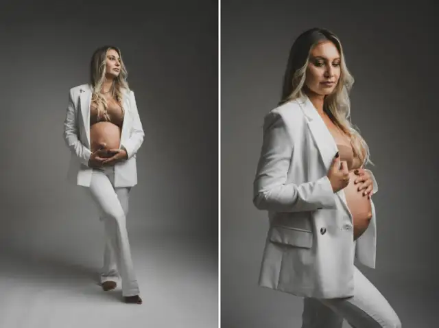 Elegancka sesja ciążowa w domu: przyszła mama w białym garniturze czule obejmuje brzuszek. Pomysły na stylowe zdjęcia.