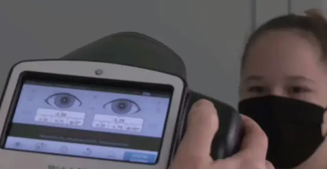 Osoba w masce na twarzy bada wzrok za pomocą urządzenia z ekranem wyświetlającym oczy i parametry.