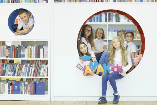 Dzieci z radością pozują z literami "AMAKids" w bibliotece.