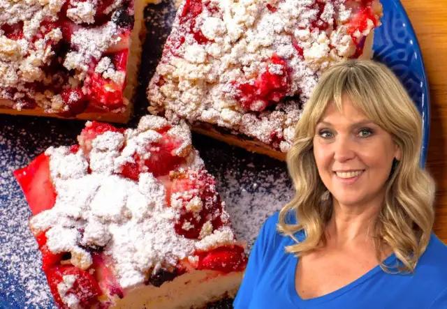 Ciasto drożdżowe bez wyrabiania Ewy Wachowicz z owocami i kruszonką, posypane cukrem pudrem. Uśmiechnięta Ewa Wachowicz w tle.