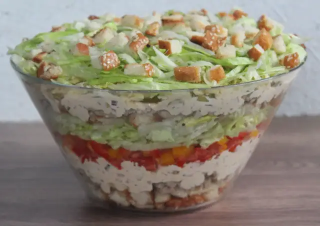 Warstwowa sałatka big mac w szklanej misie, z chrupiącymi grzankami na wierzchu.