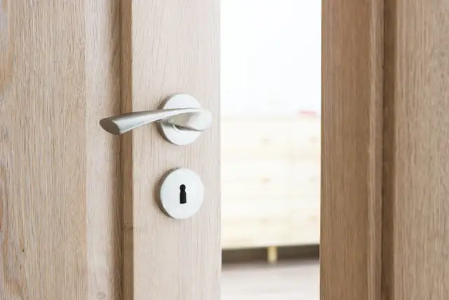 Drewniane drzwi z metalową klamką i otworem na klucz, uchylone.