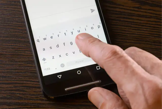 Dłoń pisze SMS-a na telefonie, klawiatura wyświetla litery. Widoczny przycisk "Polski" sugeruje, że problemem jest brak polskich znaków w sms.