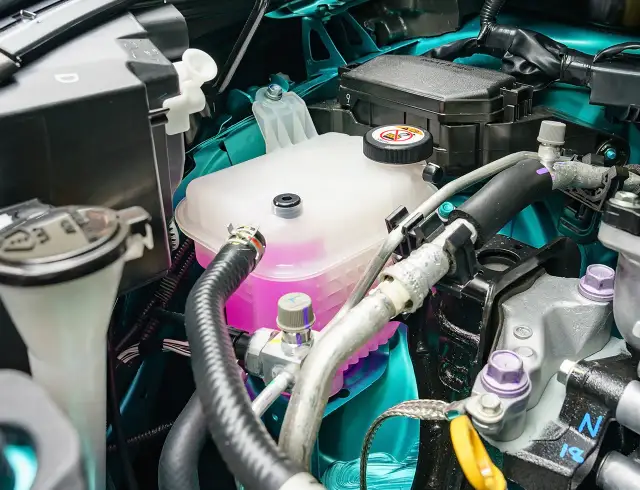 Zbiornik płynu chłodniczego z różowym płynem w komorze silnika samochodu.
