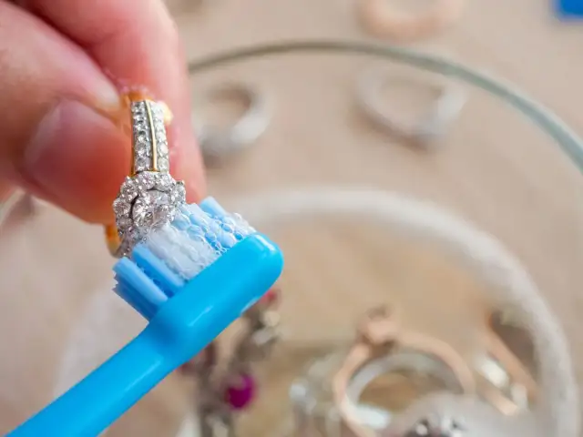 Dłoń czyści pierścionek z cyrkoniami niebieską szczoteczką z pianą.