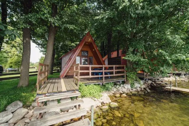 Drewniany domek w kształcie litery A nad jeziorem, z tarasem i pomostem.