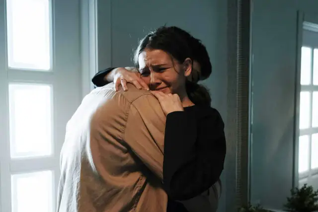 Kobieta płacze, przytulając się do ramienia innej osoby.