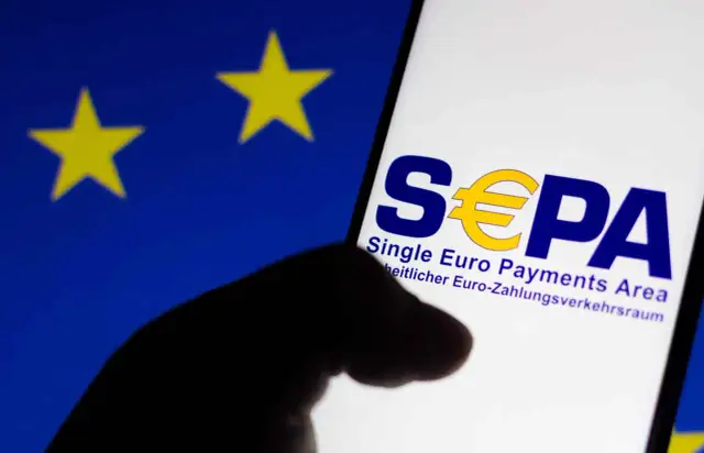 Logo SEPA na ekranie telefonu, na tle flagi UE. Czy w Albanii można płacić euro? SEPA to obszar jednolitej płatności w euro.