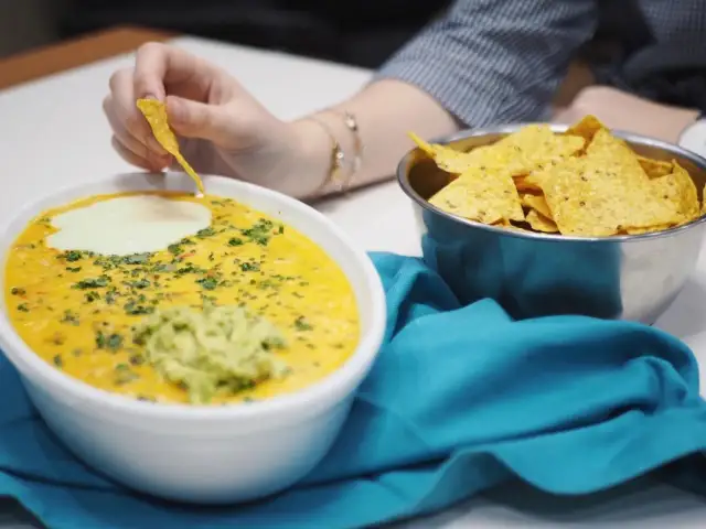 Salsa de queso cremosa con guacamole y nachos, una persona moja un totopo.