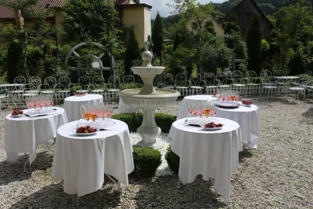 Stółki z kieliszkami i truskawkami w ogrodzie z fontanną i białymi krzesłami.