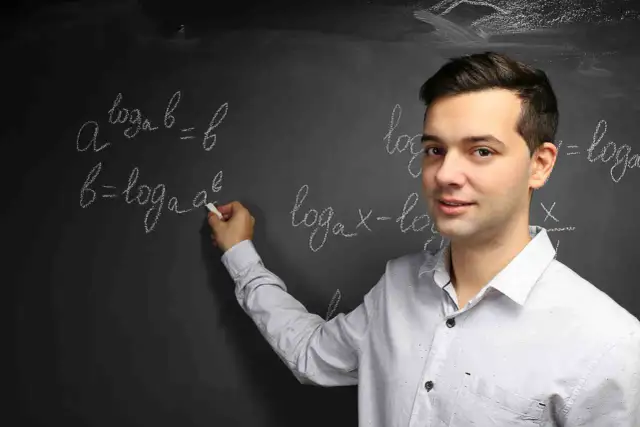 Mężczyzna pisze kredą wzory logarytmiczne na tablicy.