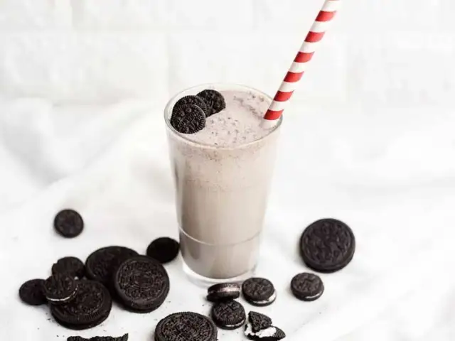 Batido cremoso de Oreo en un vaso con pajita a rayas, rodeado de galletas Oreo.