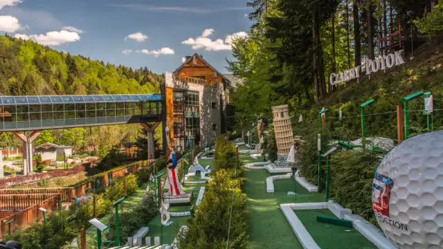 Mini golf z atrakcjami jak Krzywa Wieża w Pizie, na tle hotelu i lasu.