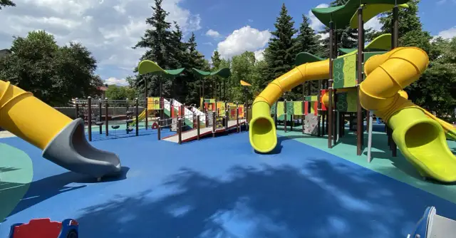 Kolorowy plac zabaw z żółtymi zjeżdżalniami i niebieską nawierzchnią.