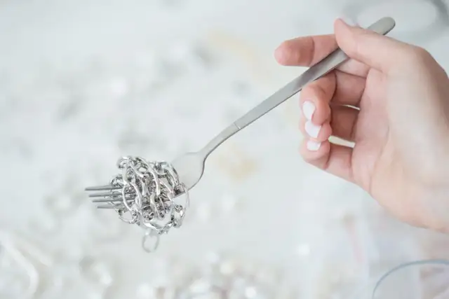 Dłoń trzyma widelec z nawiniętym na niego srebrnym łańcuszkiem.