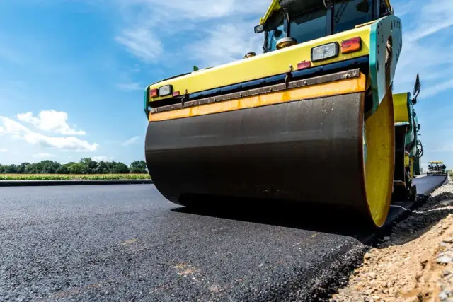 Walec drogowy ugniata świeży asfalt na tle błękitnego nieba.