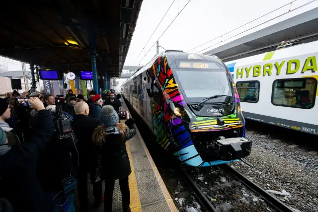 Kolorowy pociąg Hyperion na stacji, otoczony przez ludzi robiących zdjęcia.
