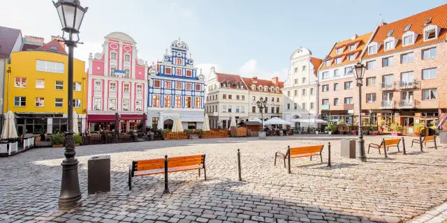 Kolorowy rynek miejski z kamienną nawierzchnią, ławkami i zabytkowymi kamienicami.