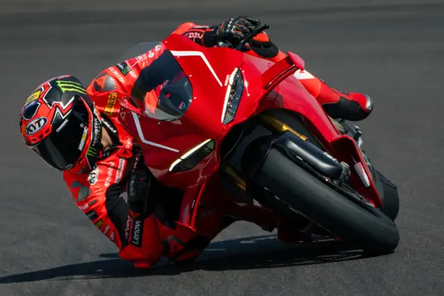 Motocyklista w czerwonym kombinezonie pochyla się na torze na swoim czerwonym Ducati Panigale V4.