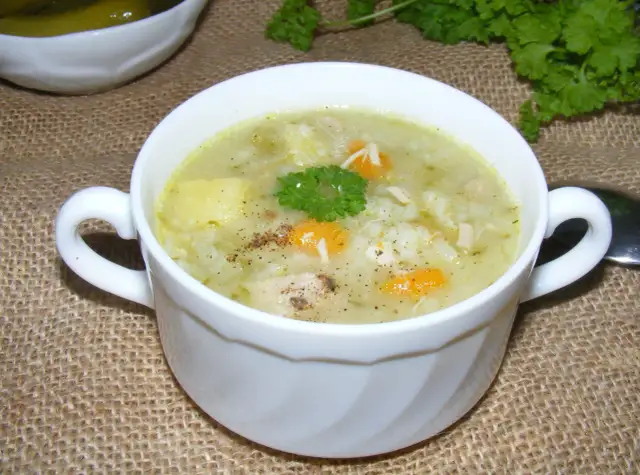 Pyszna zupa ogórkowa z ryżem, kawałkami kurczaka i marchewką, udekorowana natką pietruszki.
