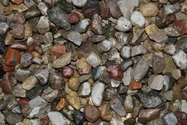Zbliżenie na mokry żwir o różnej wielkości i kolorach, od jasnoszarego do czerwono-brązowego.
