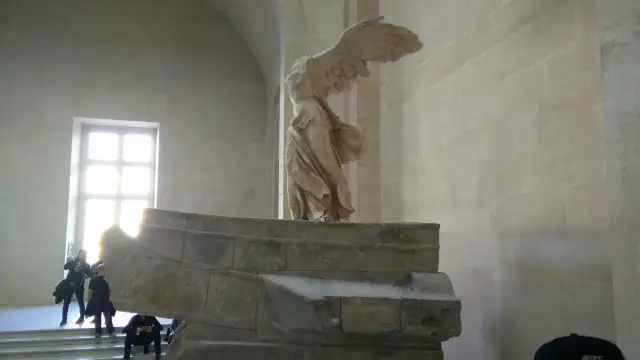 Skrzydlata Nike, symbol zwycięstwa, niczym mit, unosi się nad kamiennym postumentem.