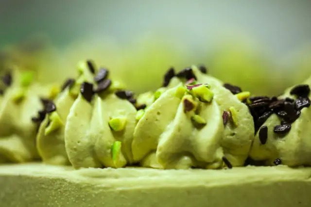 Delikatna masa pistacjowa ozdobiona kawałkami pistacji i czekolady, tworząca apetyczny deser.